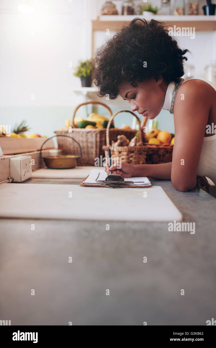 Image de jeune femme africaine le calcul des frais engagés sur un pavé d'écriture. Bar à jus féminin comptabilité propriétaire au guichet. Bref Femme Banque D'Images