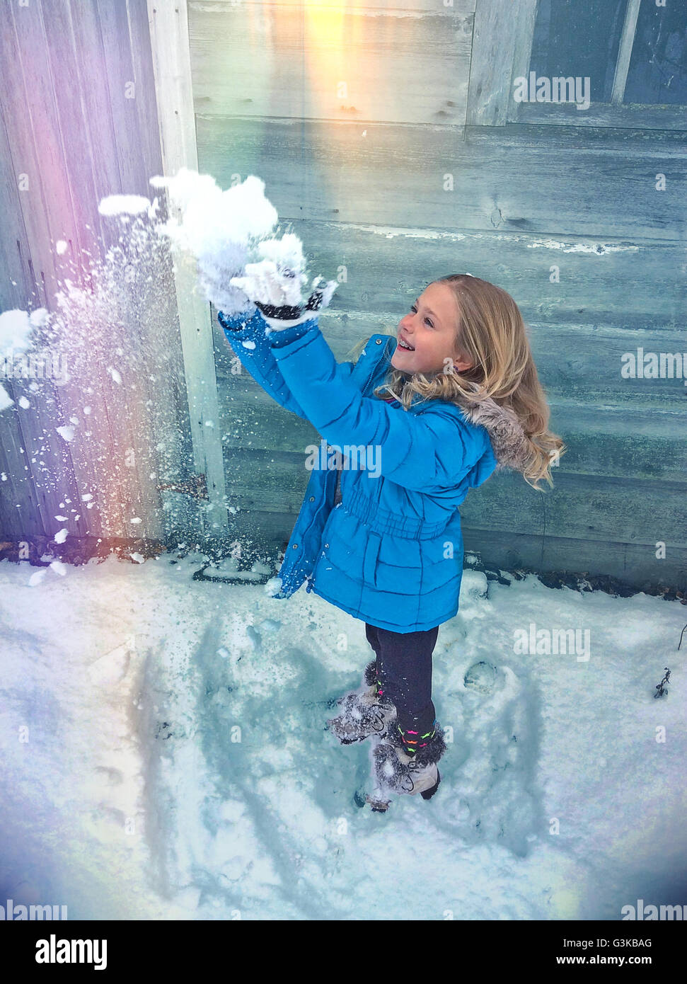 Petite blonde woman throwing snow en l'air avec l'effet arc-en-ciel. Banque D'Images