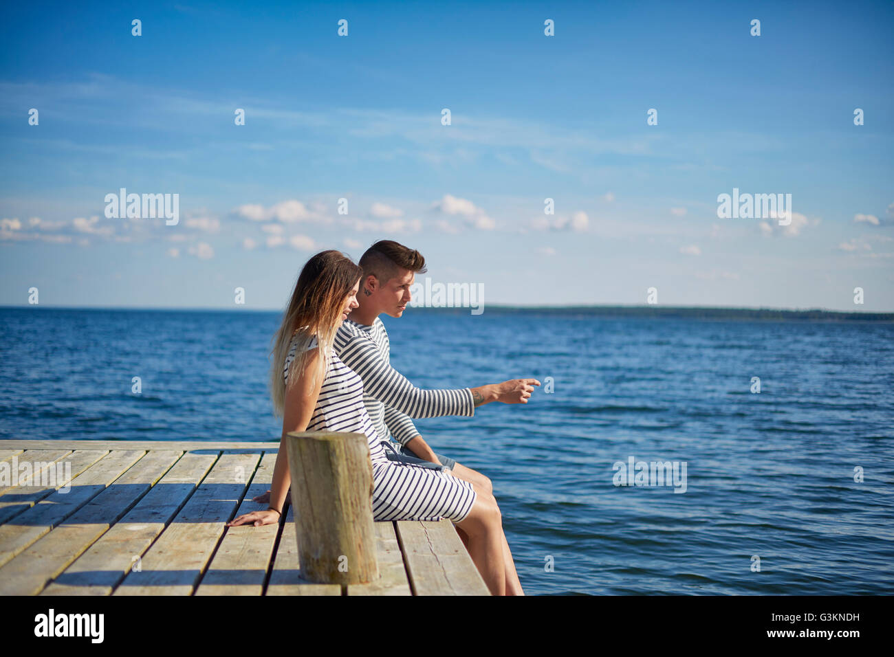Couple sitting on wooden pier, looking at view Banque D'Images