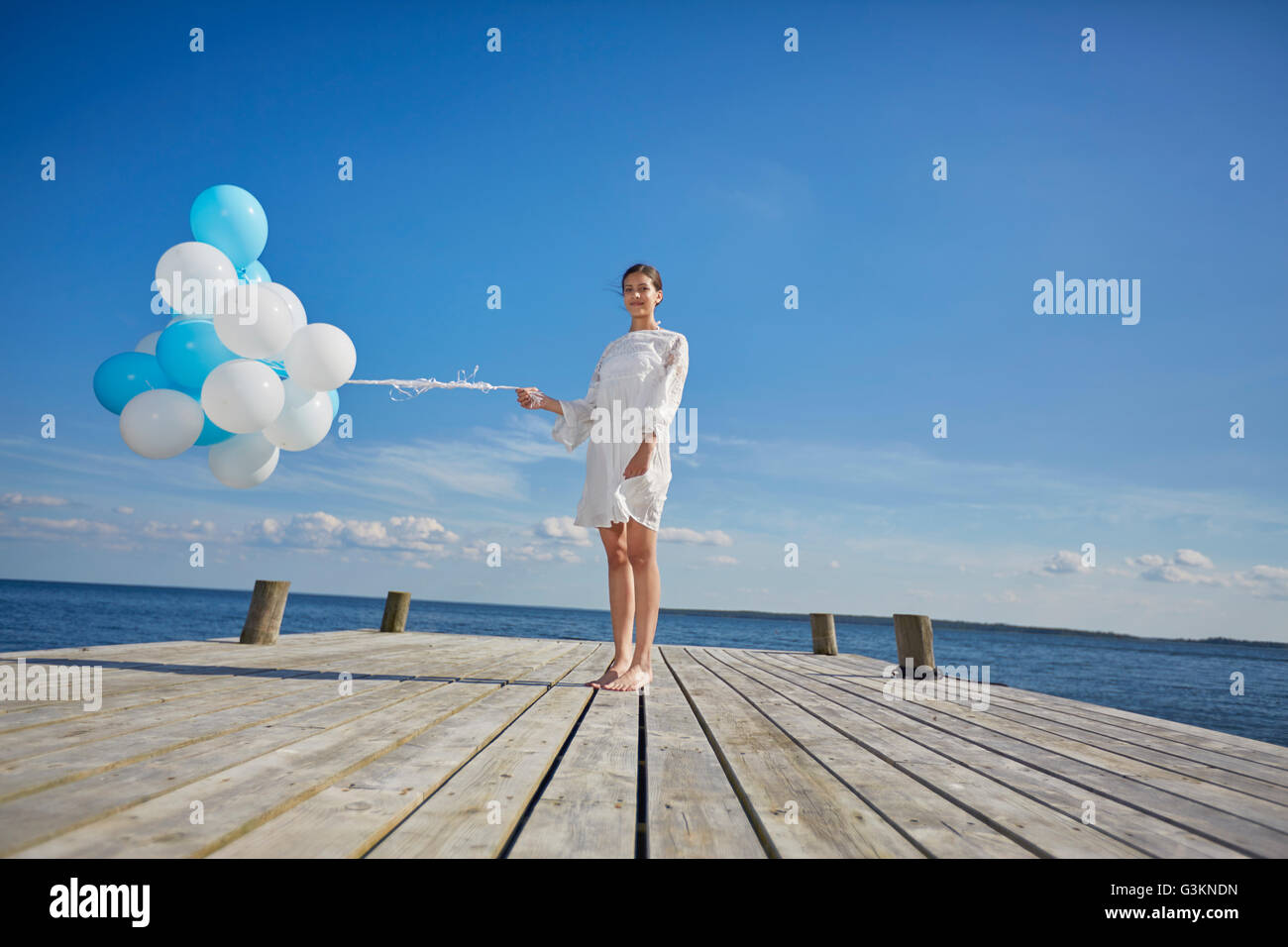 Portrait de jeune femme, debout sur la jetée en bois, holding bunch of balloons Banque D'Images