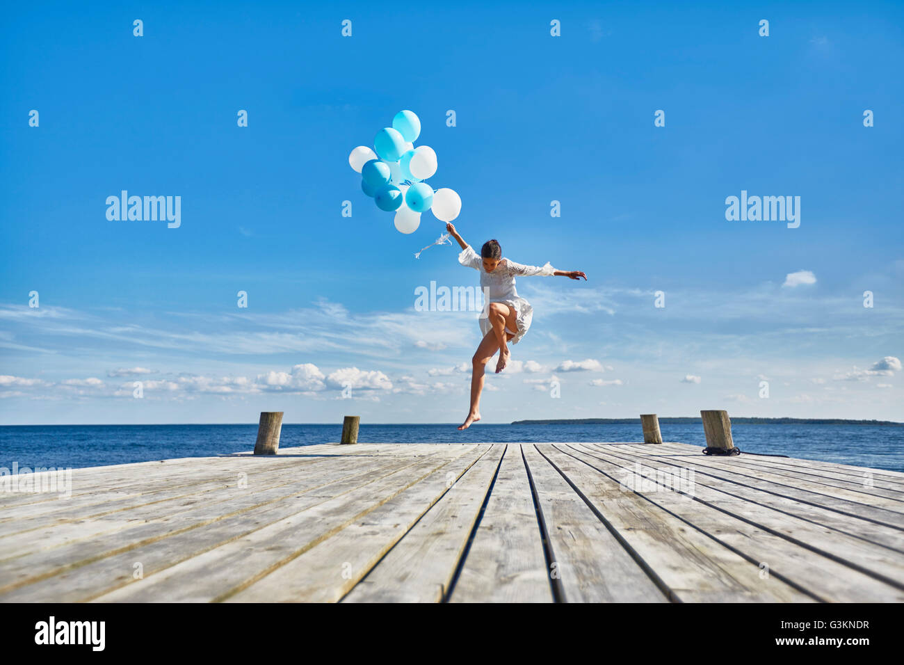 Jeune femme dansant sur jetée en bois, holding bunch of balloons Banque D'Images