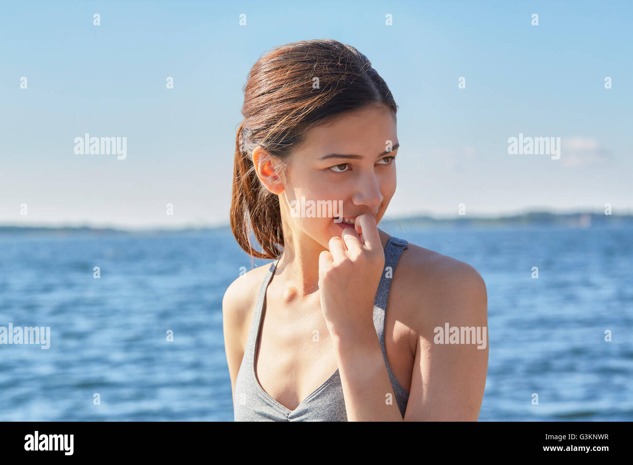 La femme en face de l'océan avec le doigt dans la bouche à l'écart Banque D'Images
