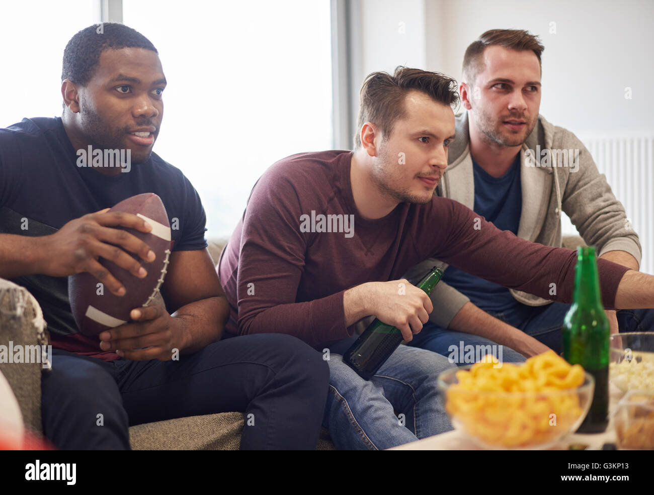 Groupe d'hommes holding ball regarder du sport à la télévision avec des collations et des bières Banque D'Images