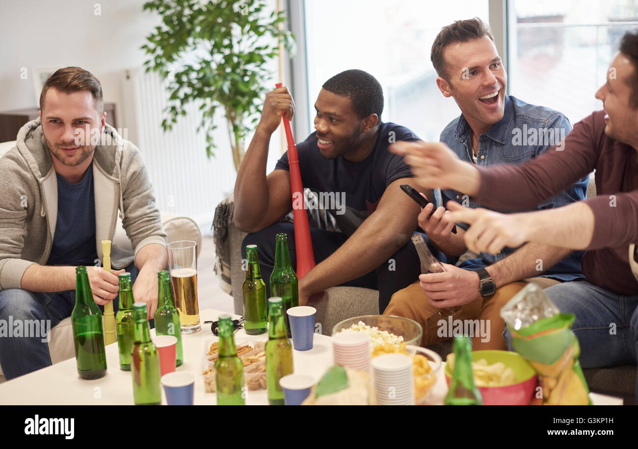 Groupe d'hommes dans le salon assis autour d'une table avec des bouteilles de bière et des collations de parler, smiling Banque D'Images