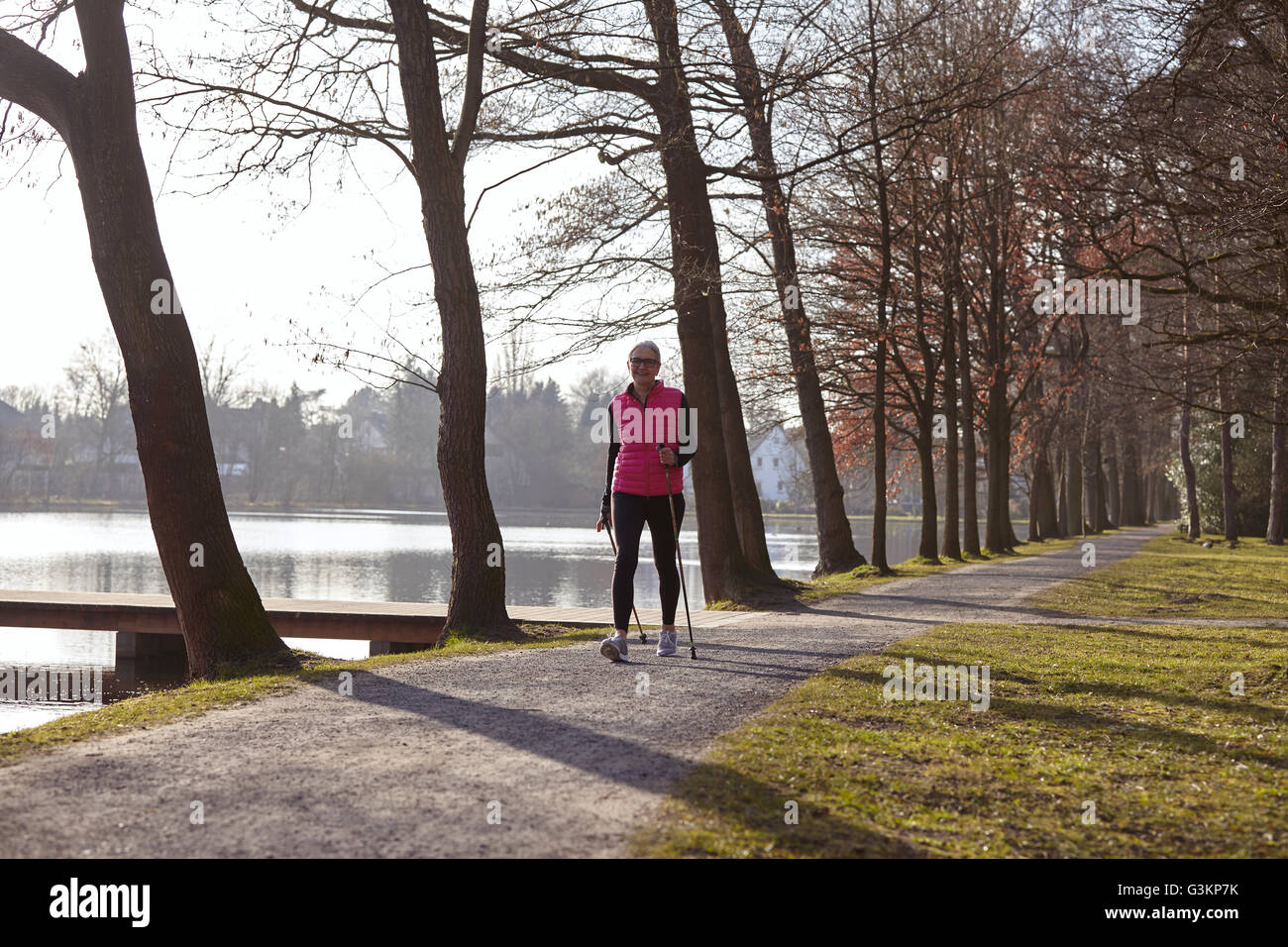 Femme de la marche nordique sur chemin bordé d'arbres par pond Banque D'Images