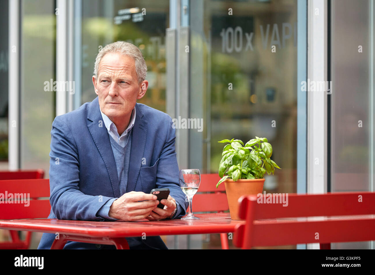 Homme mature avec attente smartphone at sidewalk cafe Banque D'Images