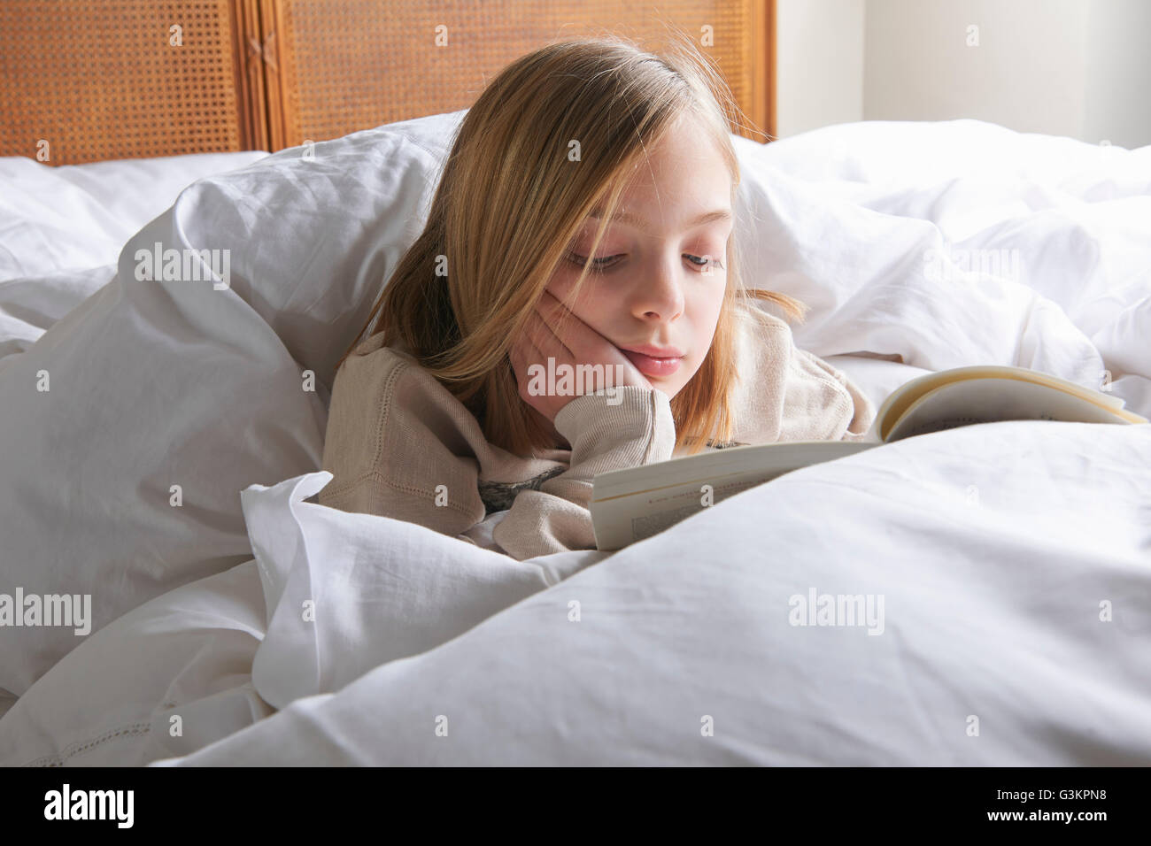 Fille aux cheveux blonds reading book in bed Banque D'Images