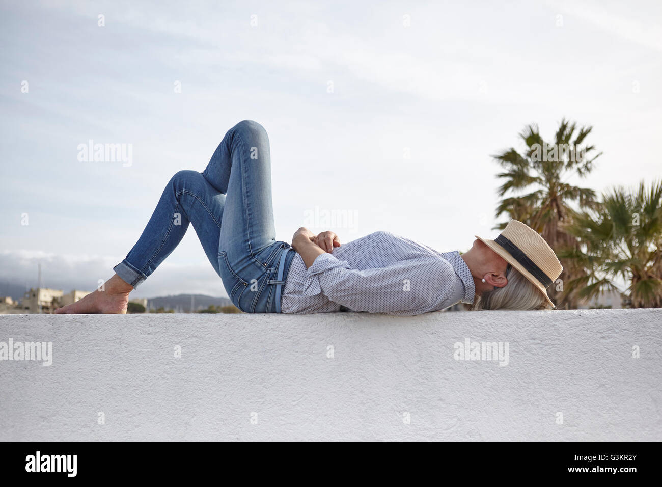 Young woman lying on wall, hat covering face Banque D'Images