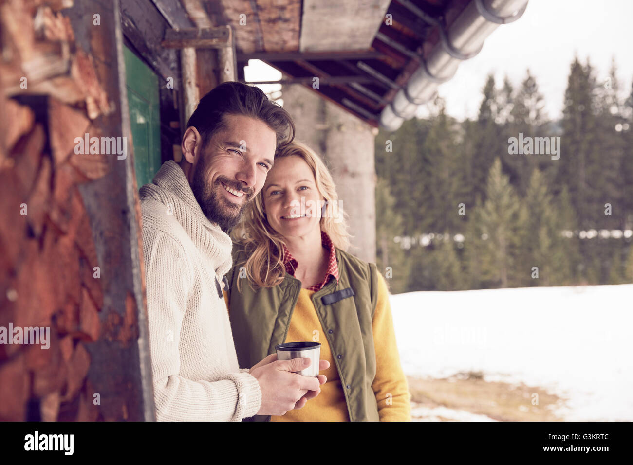 Portrait of couple standing en dehors de log cabin en hiver, Elmau, Bavière, Allemagne Banque D'Images