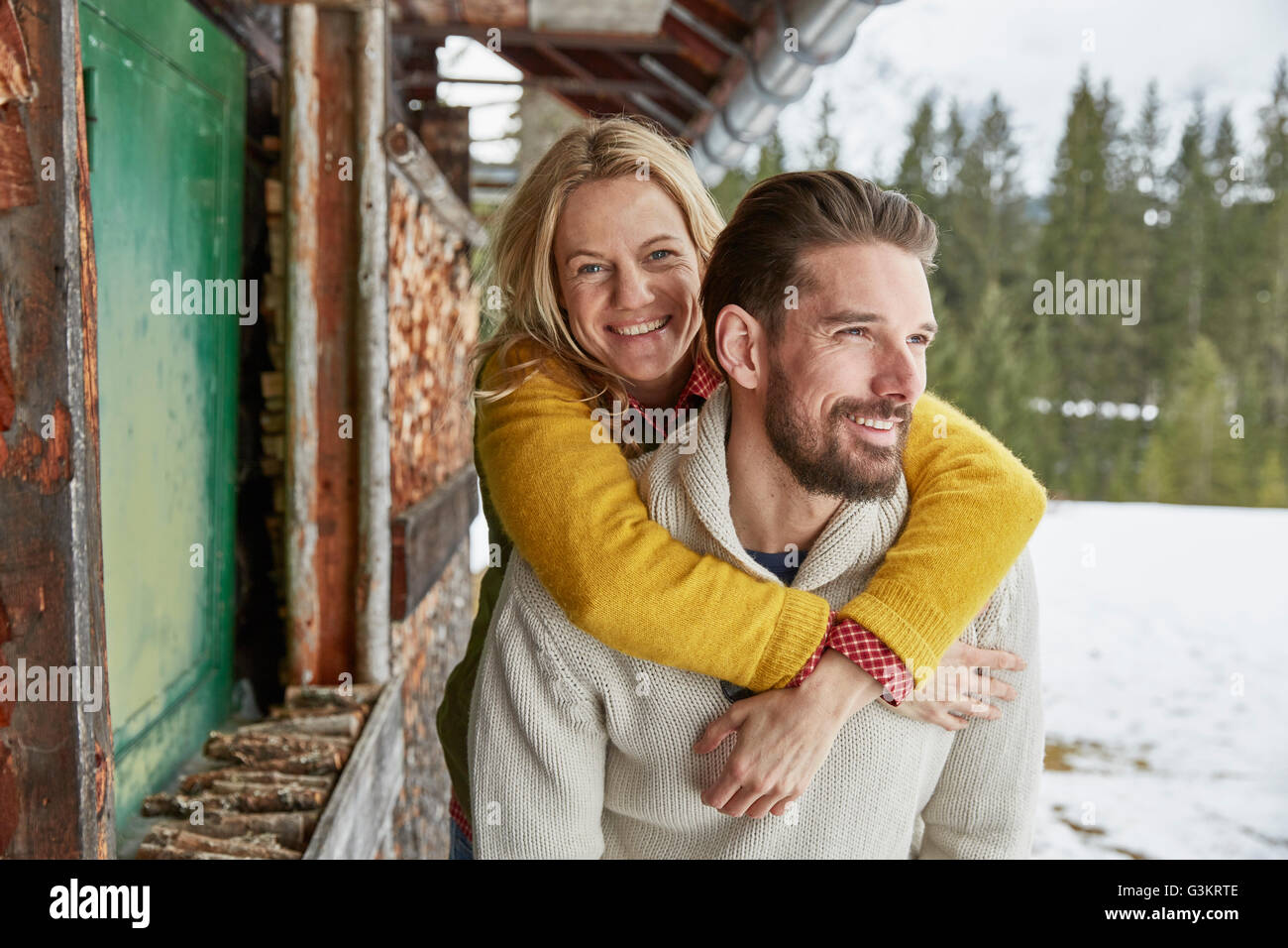 Young man giving girlfriend piggyback à l'extérieur de log cabin, Elmau, Bavière, Allemagne Banque D'Images