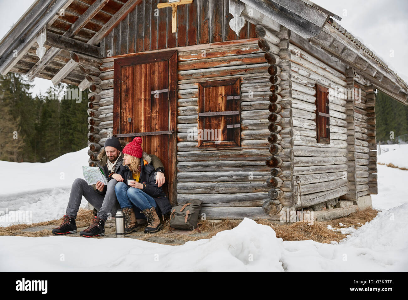 Couple assis dehors log cabin en hiver, Elmau, Bavière, Allemagne Banque D'Images