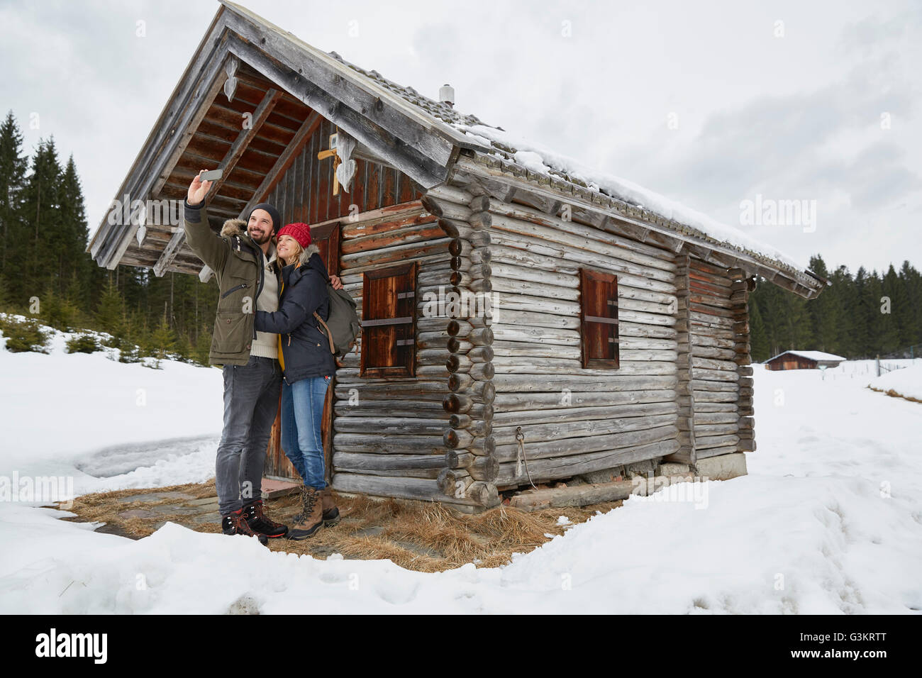 Couple en tenant l'extérieur selfies smartphone log cabin en hiver, Elmau, Bavière, Allemagne Banque D'Images
