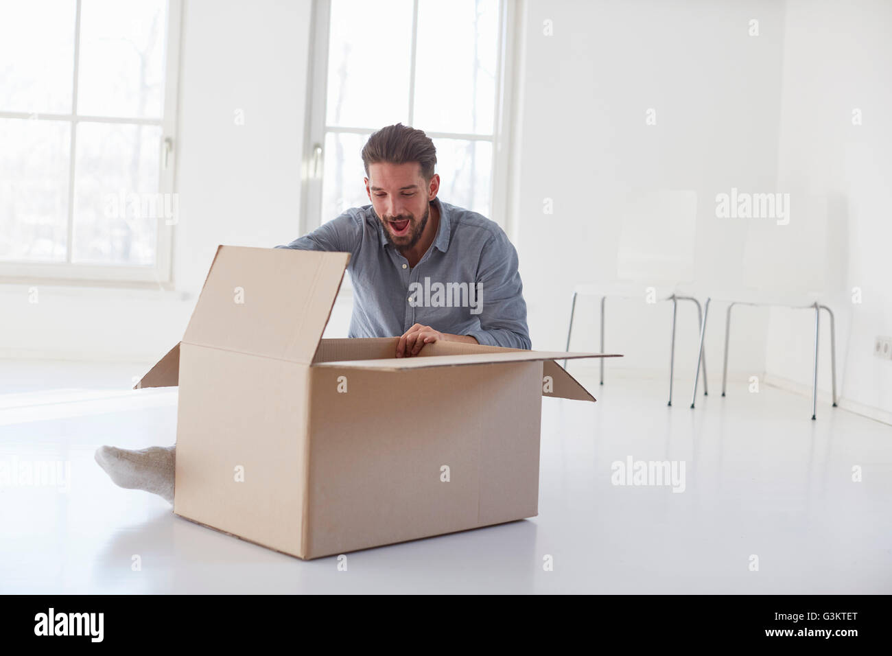Jeune homme assis sur ouverture de plancher boîte carton in new house Banque D'Images