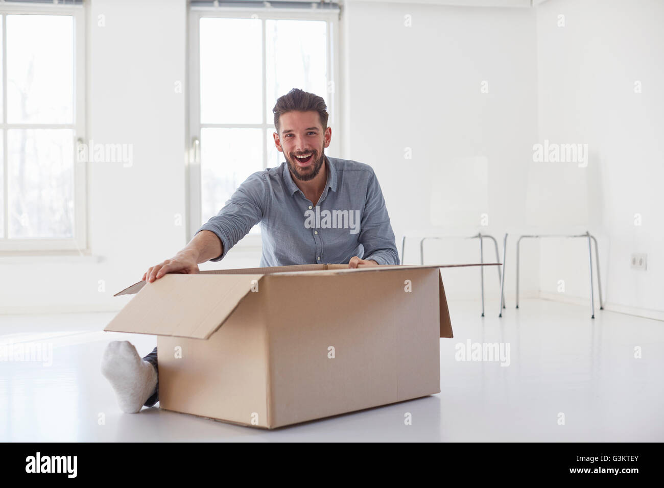 Portrait de jeune homme assis sur ouverture de plancher boîte carton in new house Banque D'Images