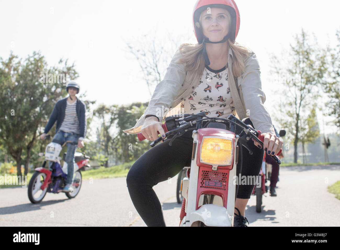 Groupe d'amis équitation cyclomoteurs le long de la route, les jeunes femmes rider en premier plan Banque D'Images