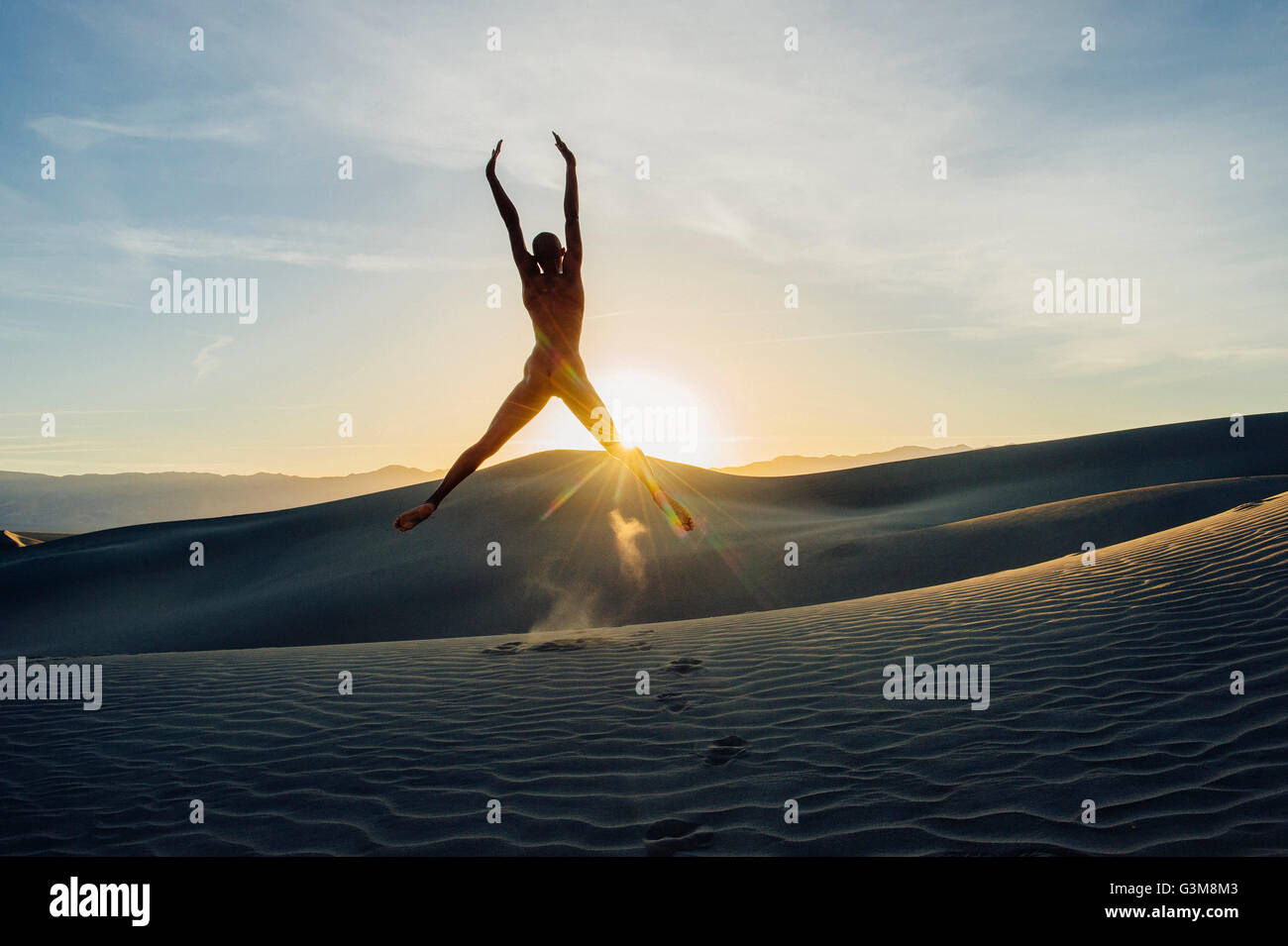 Femme nue dans le désert bras levés en l'air saut Banque D'Images