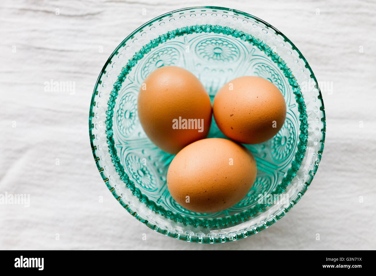 Oeufs frais de la ferme dans un bol turquoise avec fond blanc texturé Banque D'Images