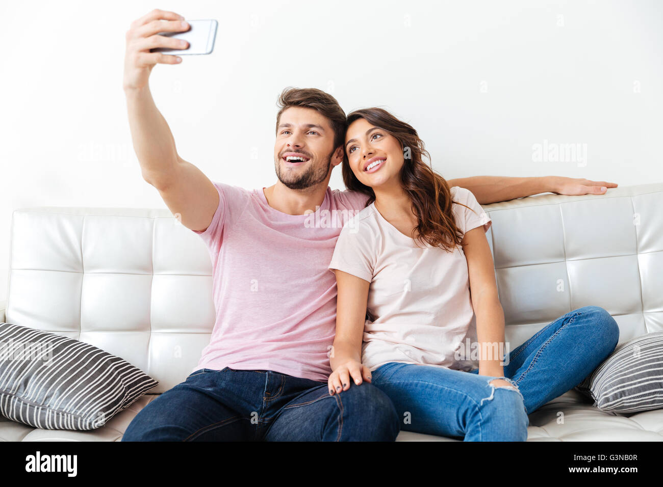 Beau jeune couple fait l'utilisation d'un smartphone selfies smiling while sitting on sofa isolé sur fond blanc Banque D'Images