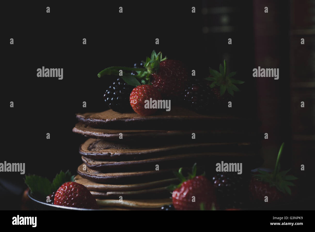 Des crêpes dans la casserole rouillée avec des fraises et des mûres et les vieux livres en arrière-plan avec la lumière mystique Banque D'Images