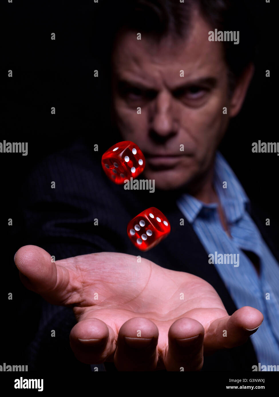 L'homme, d'un costume sans cravate, holding red dices, prendre un risque sur un fond noir Banque D'Images
