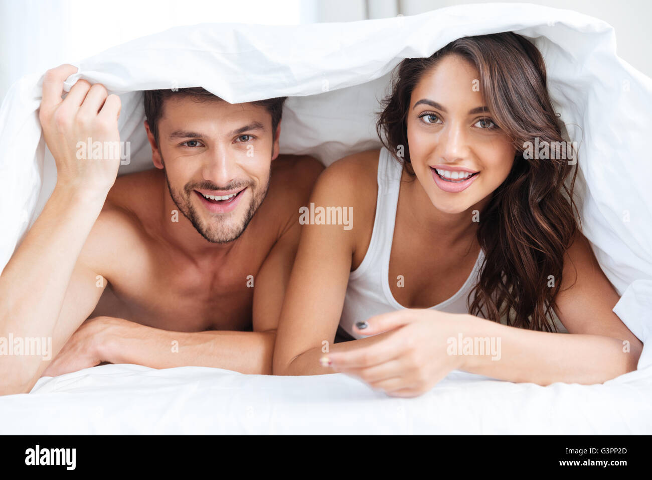 Couple heureux au lit recouvert d'une couverture sur la tête et de parler à la maison plus de lumières fond à la maison Banque D'Images