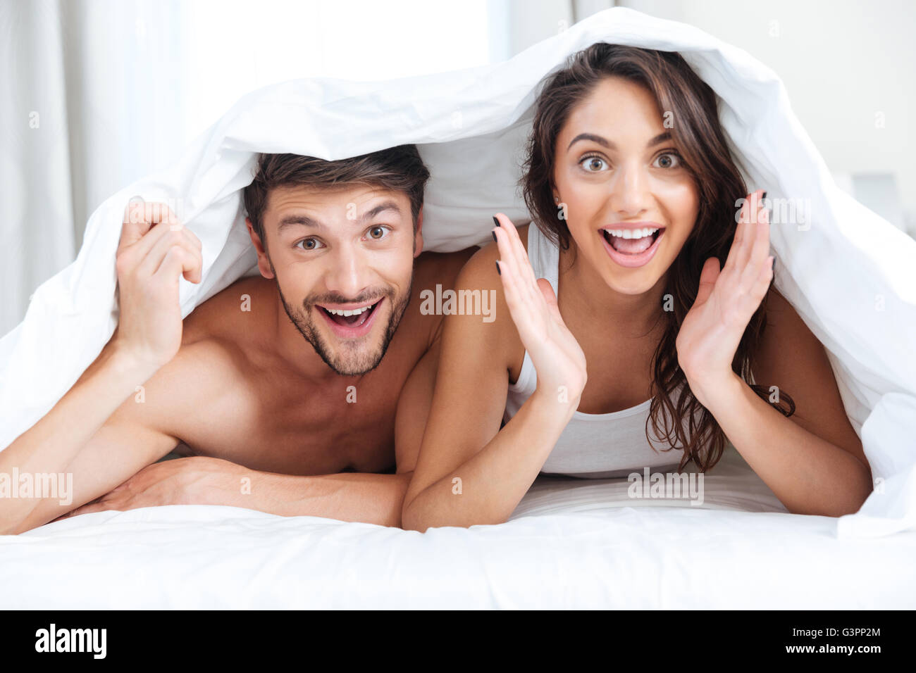 Happy smiling couple Lying in Bed covered with blanket at home Banque D'Images