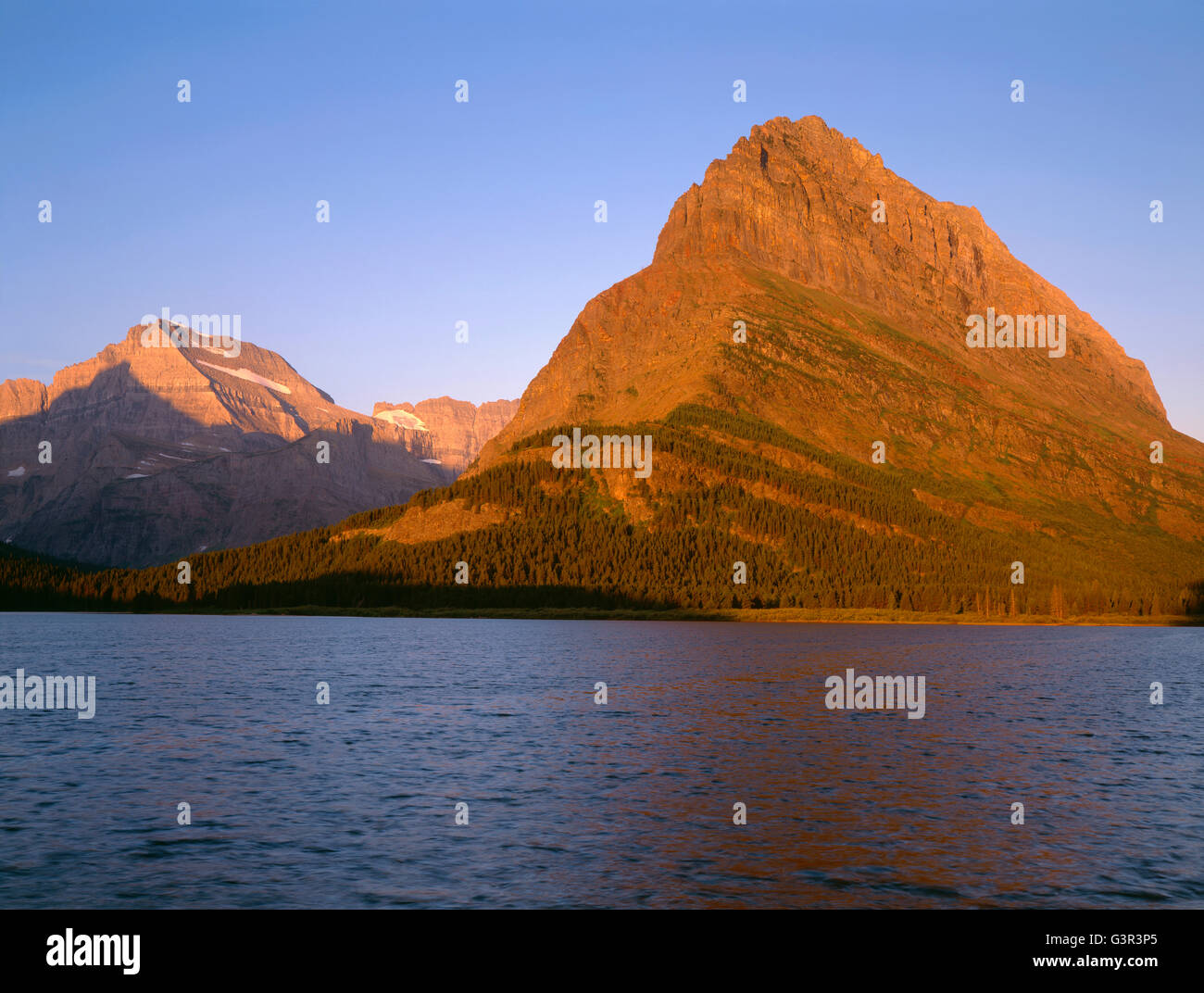 USA, Montana, le parc national des Glaciers, le lever du soleil la lumière sur Grinnell Point et plus lointain Mount Gould au-dessus du lac Swiftcurrent venteux. Banque D'Images