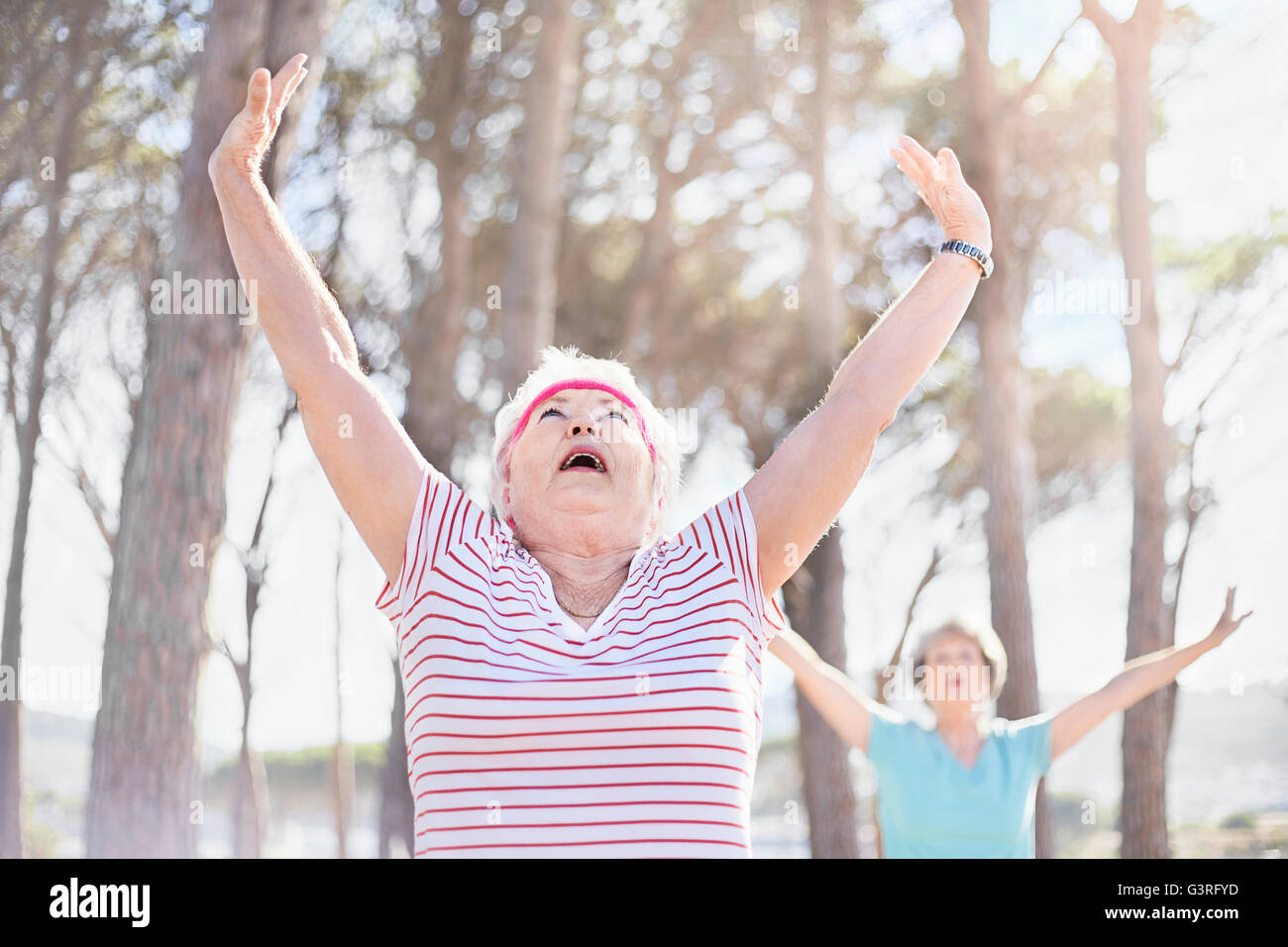 Senior woman stretching arms overhead en yoga class in sunny park Banque D'Images