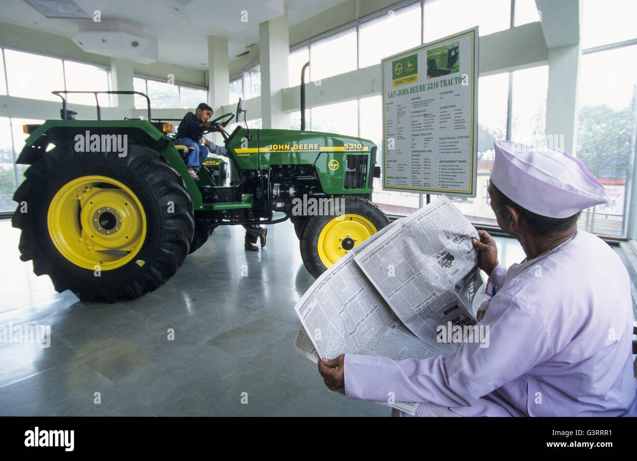 INDE, Maharashtra, Pune, concessionnaire de tracteurs John Deere dans le village, tracteur John Deere 5310 dans la salle d'exposition, agriculteur avec journal , son fils jouant sur le tracteur Banque D'Images