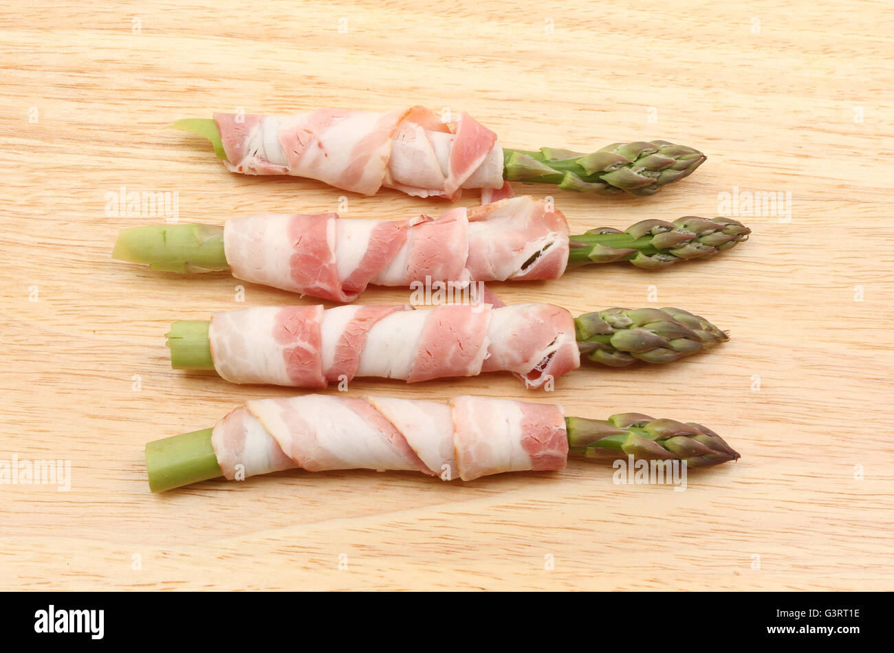 Asperges avec de la pancetta sur une planche à découper en bois Banque D'Images