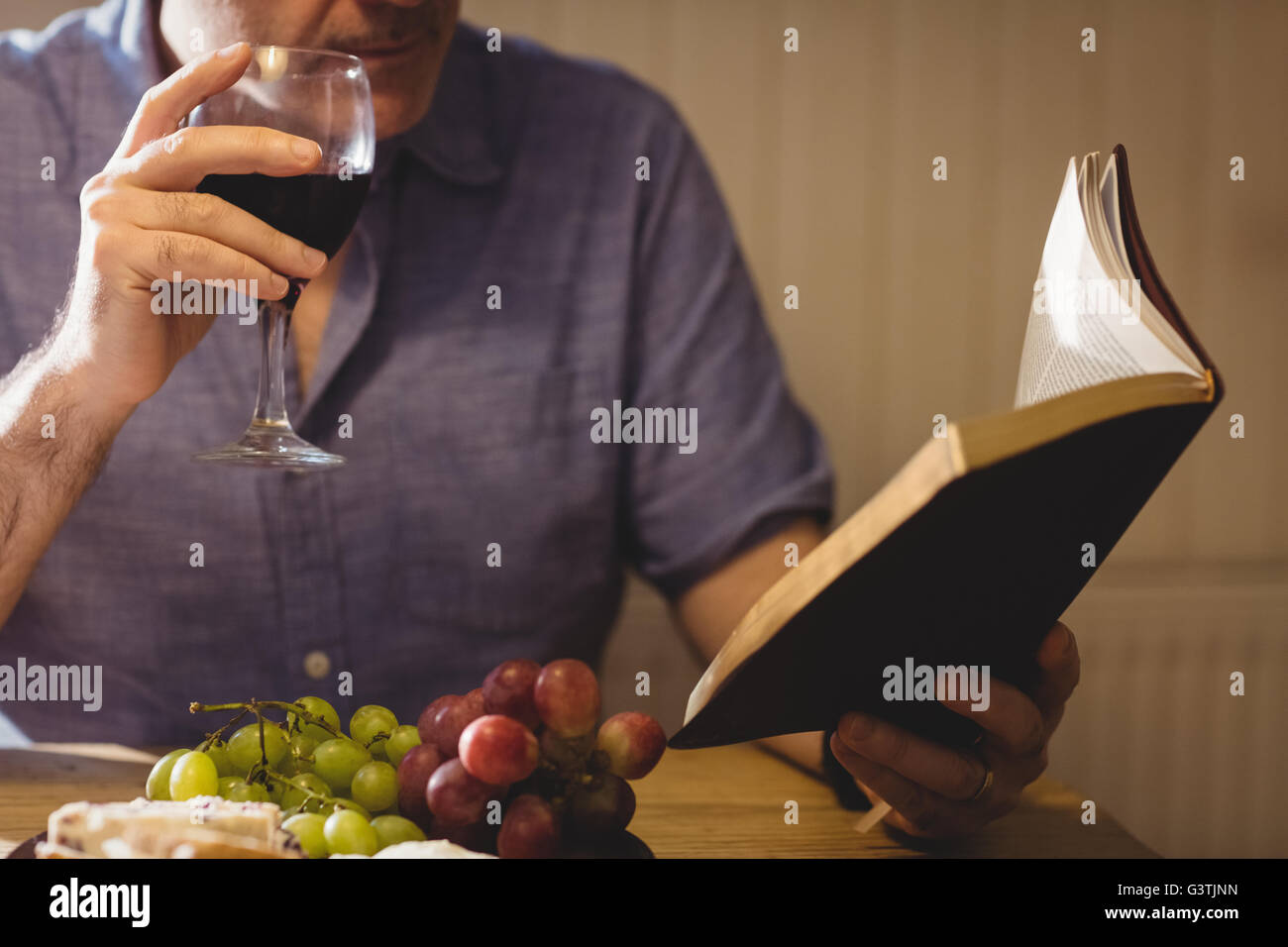Portrait de l'homme de boire dans un verre de vin tout en lisant un livre Banque D'Images
