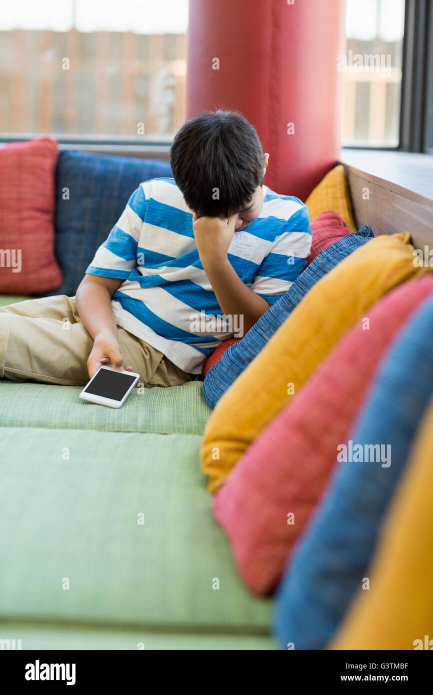 Fâché garçon assis sur un canapé et holding a mobile phone Banque D'Images