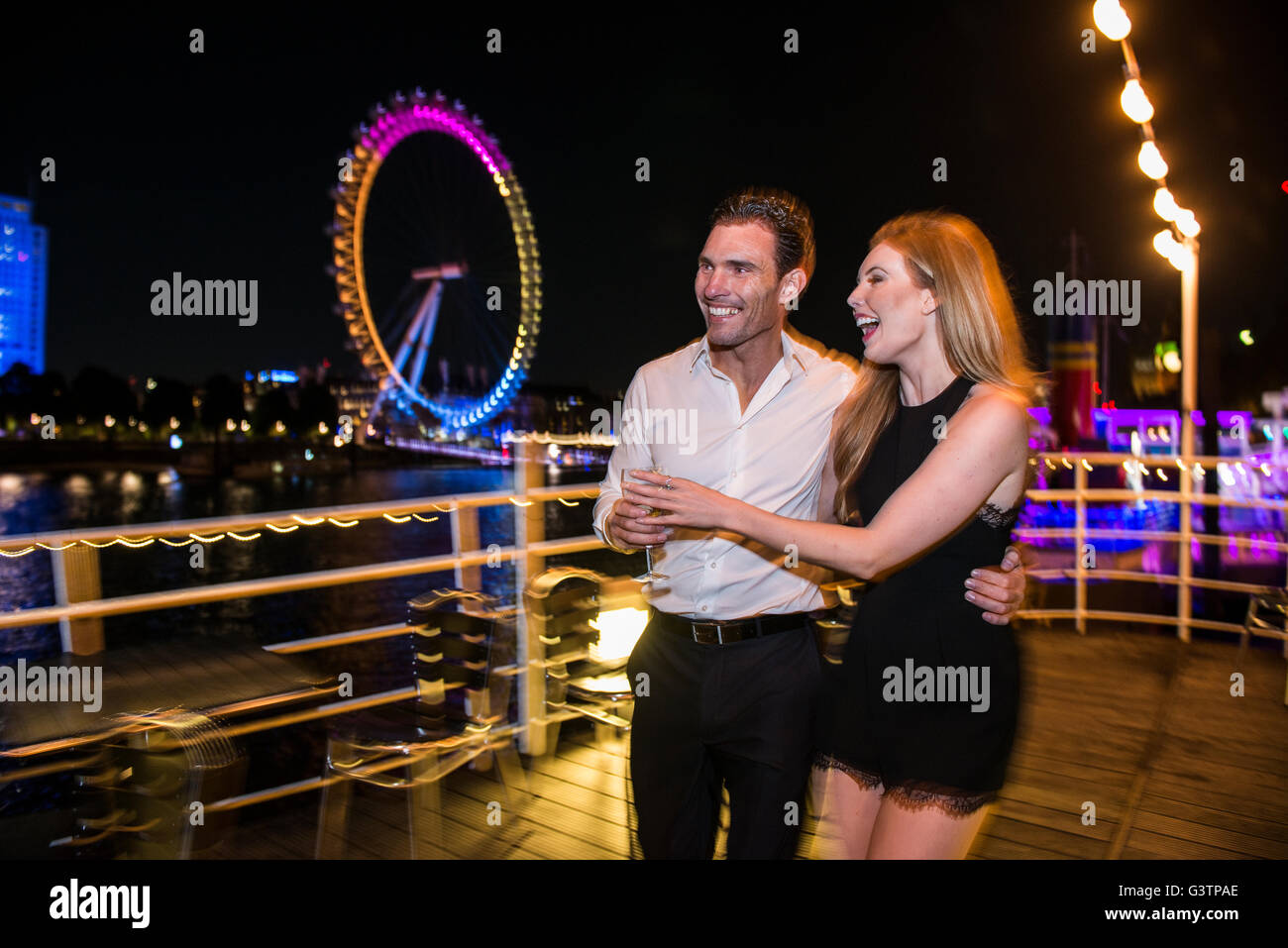 Un couple habillés de déguster une boisson sur le pont d'un bateau amarré à quai à Londres. Banque D'Images