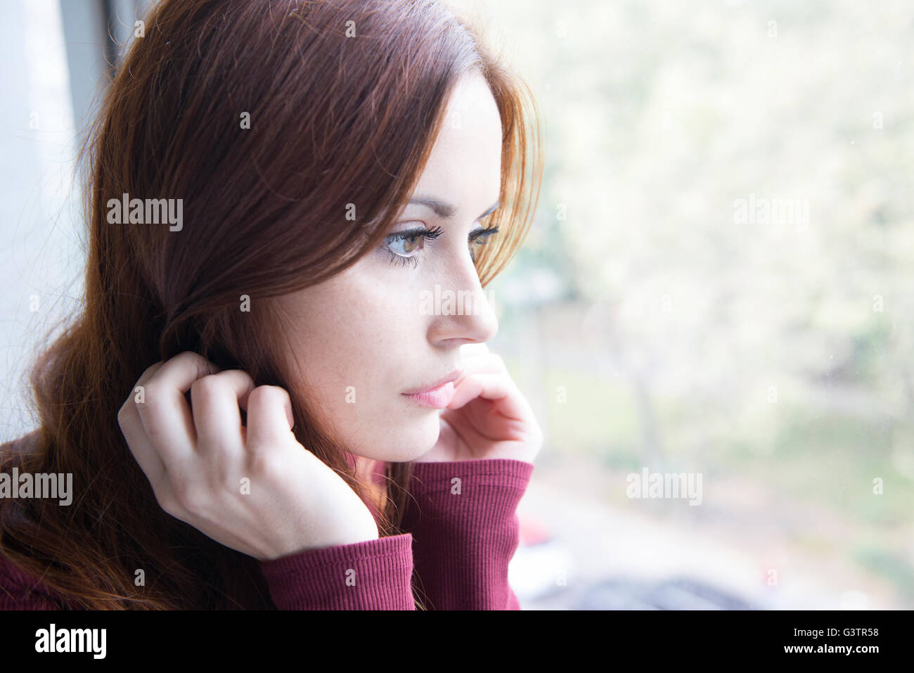 Portrait d'une belle jeune femme assise par une fenêtre. Banque D'Images