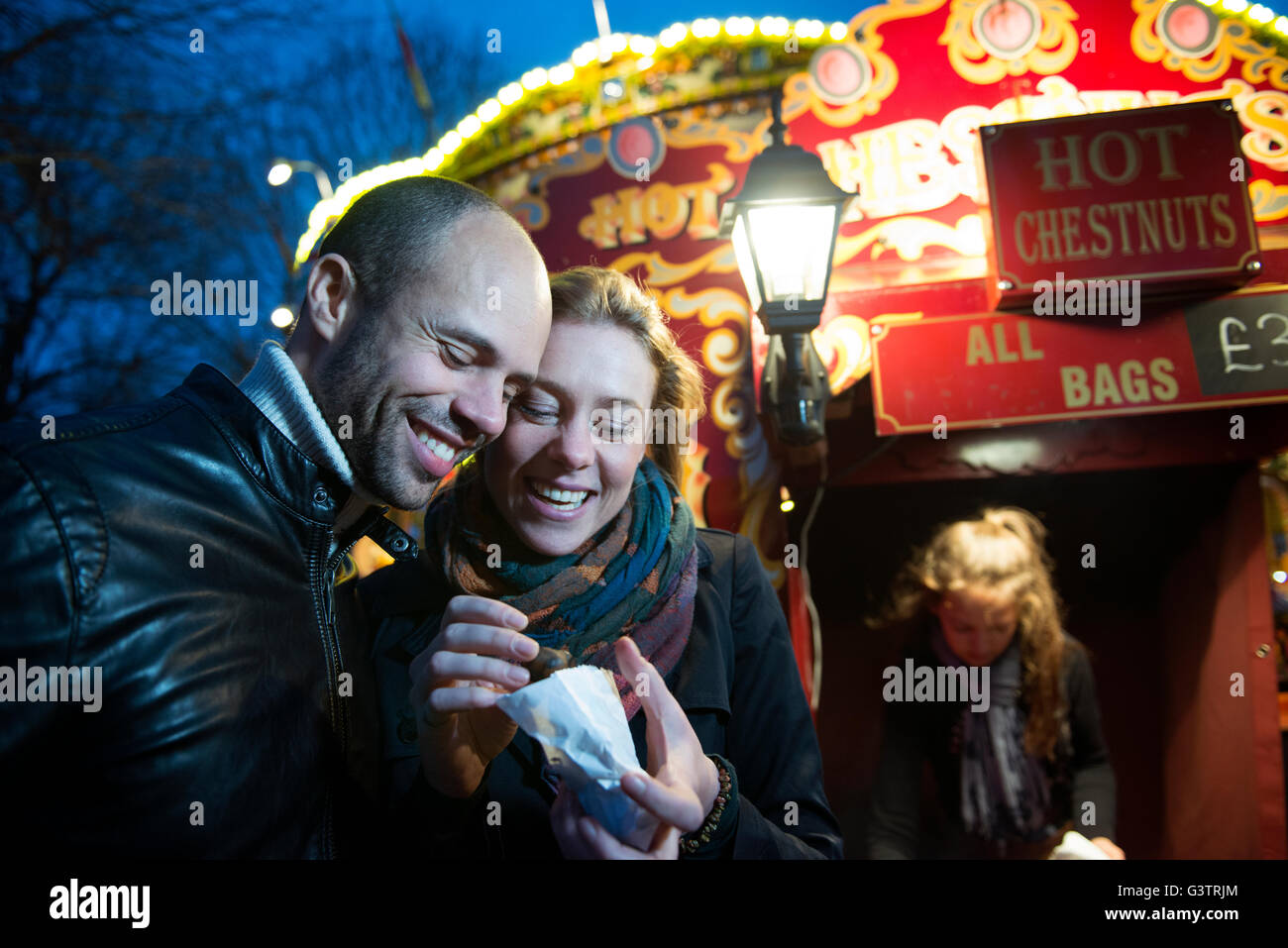 Un couple debout devant un vendeur vente de marrons chauds sur la rive sud de Londres la nuit. Banque D'Images