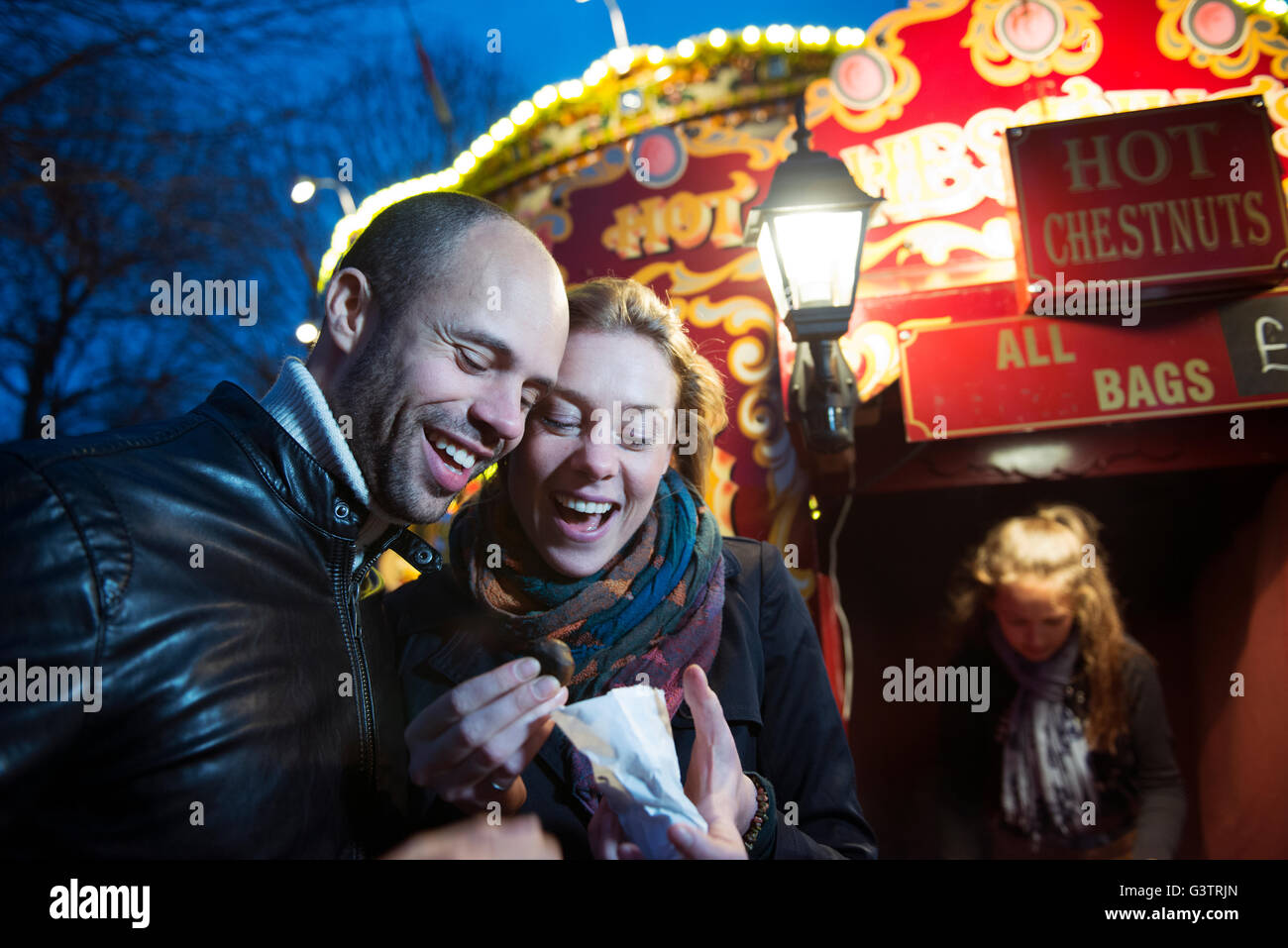 Un couple debout devant un vendeur vente de marrons chauds sur la rive sud de Londres la nuit. Banque D'Images
