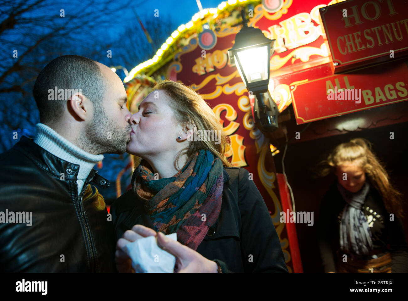 Un couple s'embrasser devant un vendeur vente de marrons chauds sur la rive sud de Londres la nuit. Banque D'Images