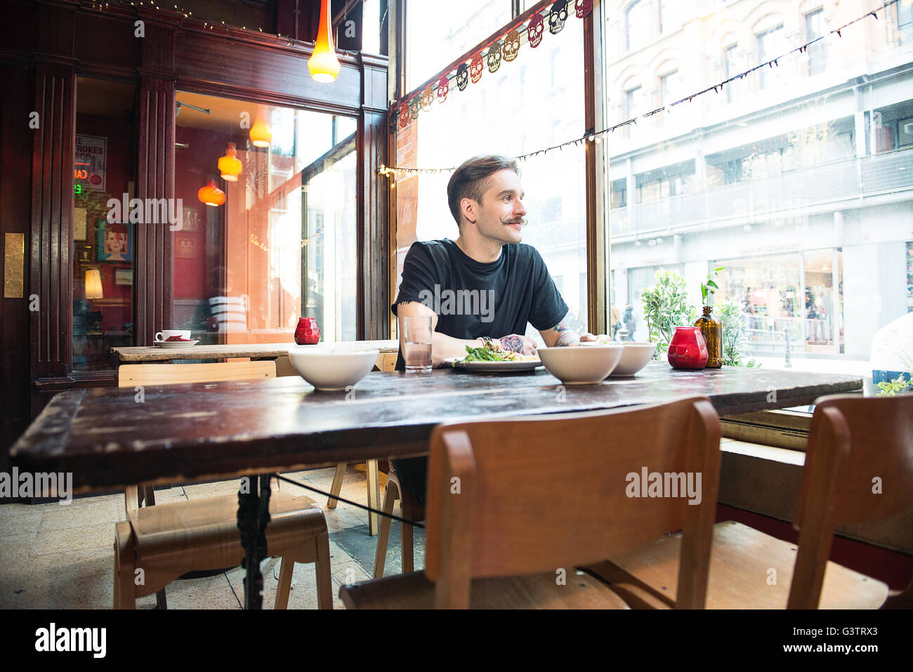 Un jeune homme assis à une table dans un café à Manchester. Banque D'Images