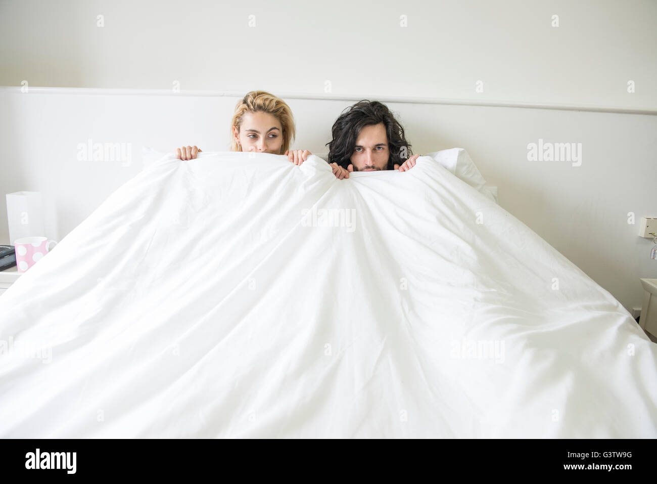Un jeune couple cool tatoué dans un lit double à l'cache avec l'appareil photo. Banque D'Images
