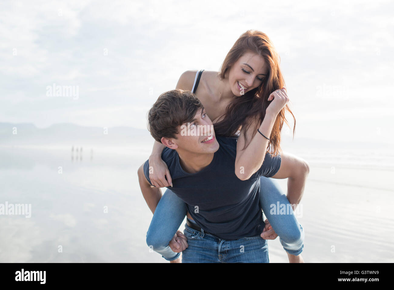 Un jeune couple jouant piggy back sur la plage à Porthmadog. Banque D'Images