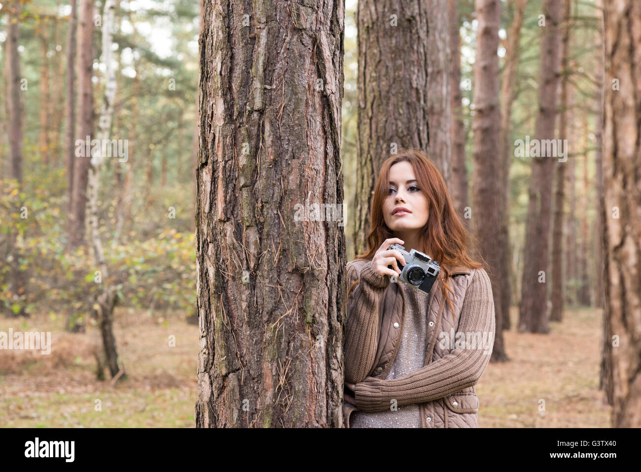 Une jeune femme à l'aide d'un appareil photo vintage dans une forêt en automne. Banque D'Images