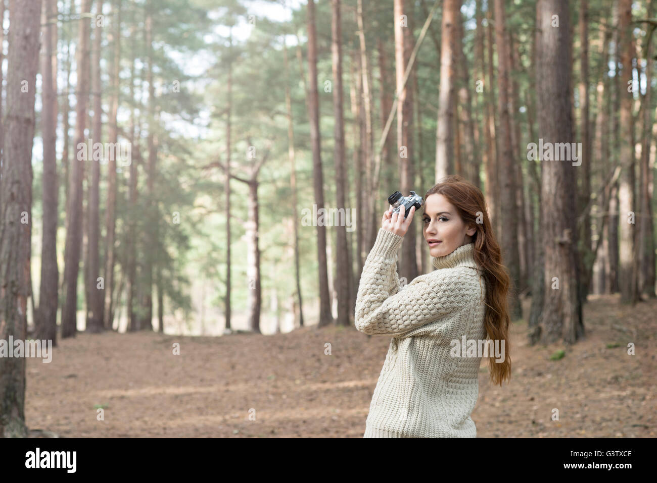 Une jeune femme à l'aide d'un appareil photo vintage dans une forêt en automne. Banque D'Images