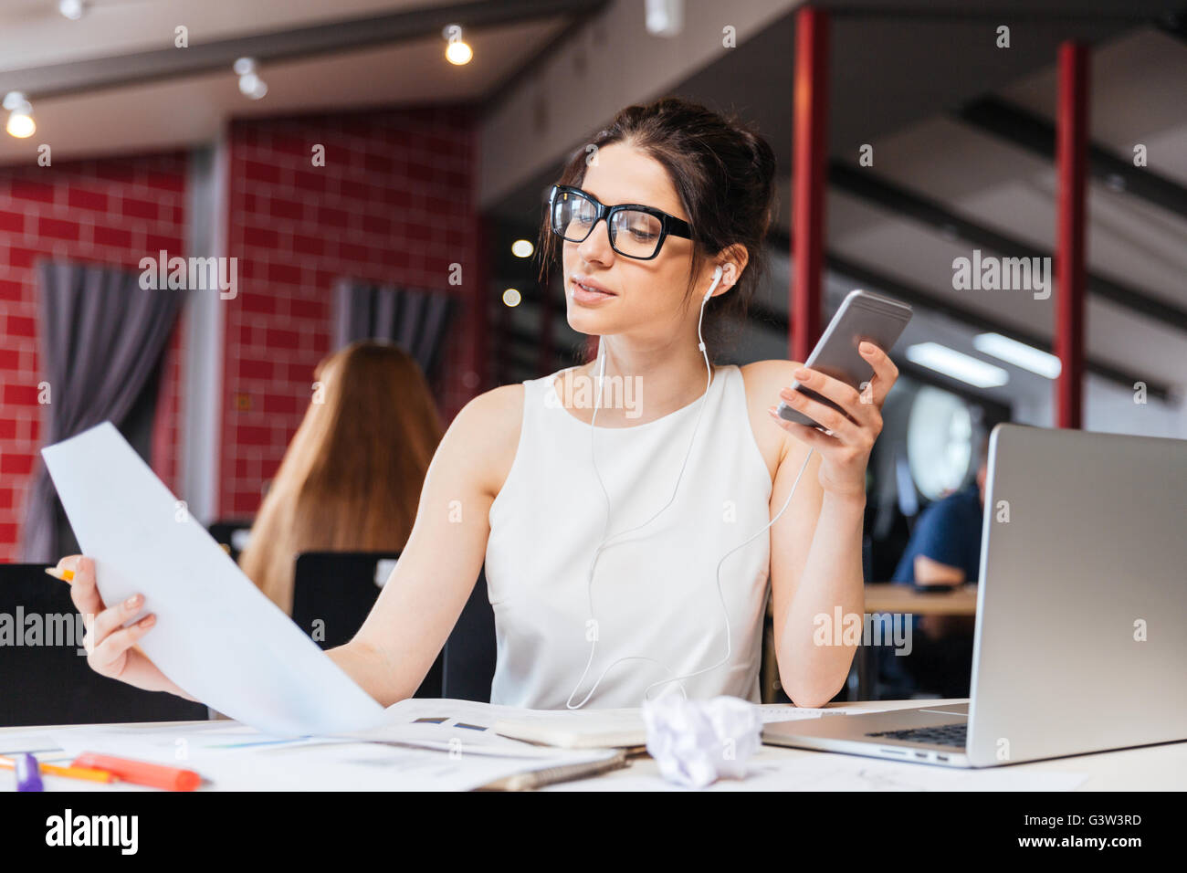 Pensive young attractive businesswoman working et écouter de la musique du smartphone in office Banque D'Images