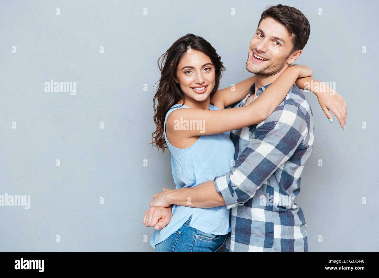 Casual young couple hugging each other and smiling at camera isolé sur fond gris Banque D'Images