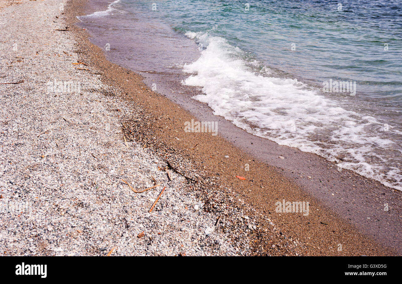 Plage de sable grossier et de pierres avec de petites vagues se briser. Banque D'Images