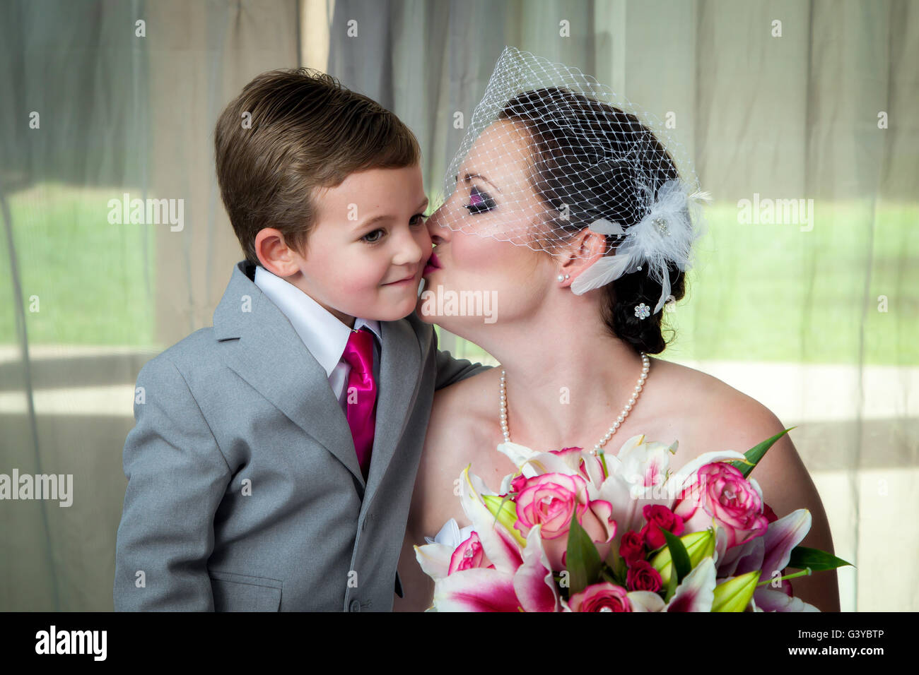 Une jeune mariée embrasse son fils le jour de son mariage dans son portrait avant-mariage. Elle tient son bouquet et il se penche pour un baiser. Banque D'Images