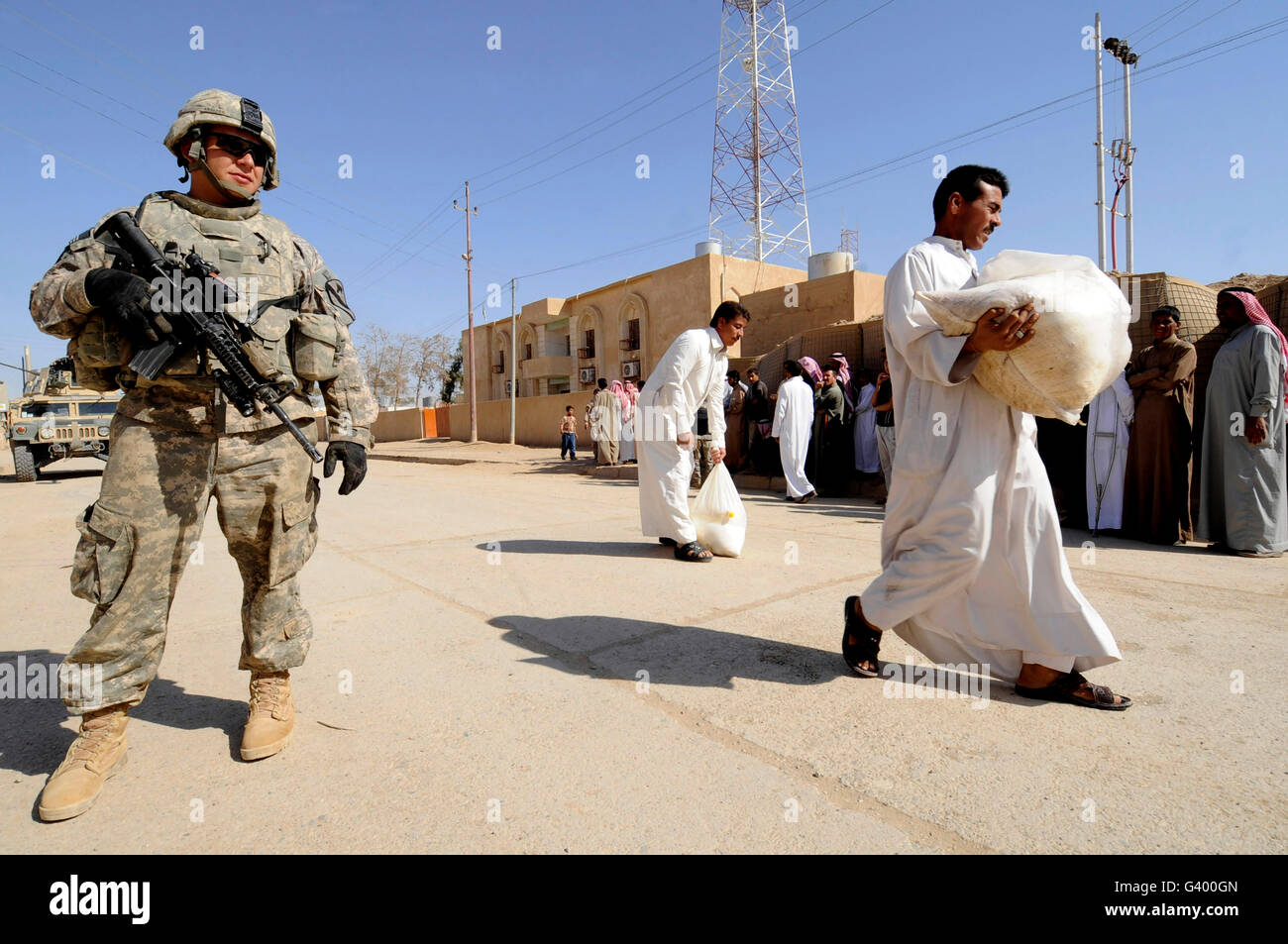 Un soldat monte la garde de l'armée américaine que les habitants de marche avec l'approvisionnement en denrées alimentaires. Banque D'Images