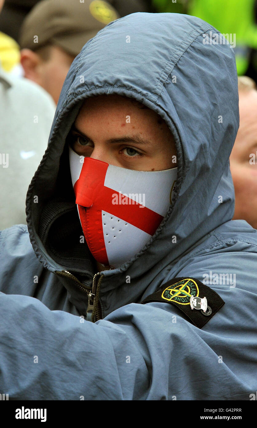 Un jeune homme couvre son visage lorsqu'il rejoint un grand groupe de membres de la Ligue de défense anglaise qui protestent sur la place St George, lors de leur manifestation à Luton cet après-midi. Banque D'Images