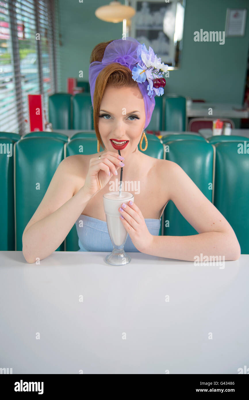 Look années 60 pin up girl dans un restaurant américain de boire un milk-shake Banque D'Images