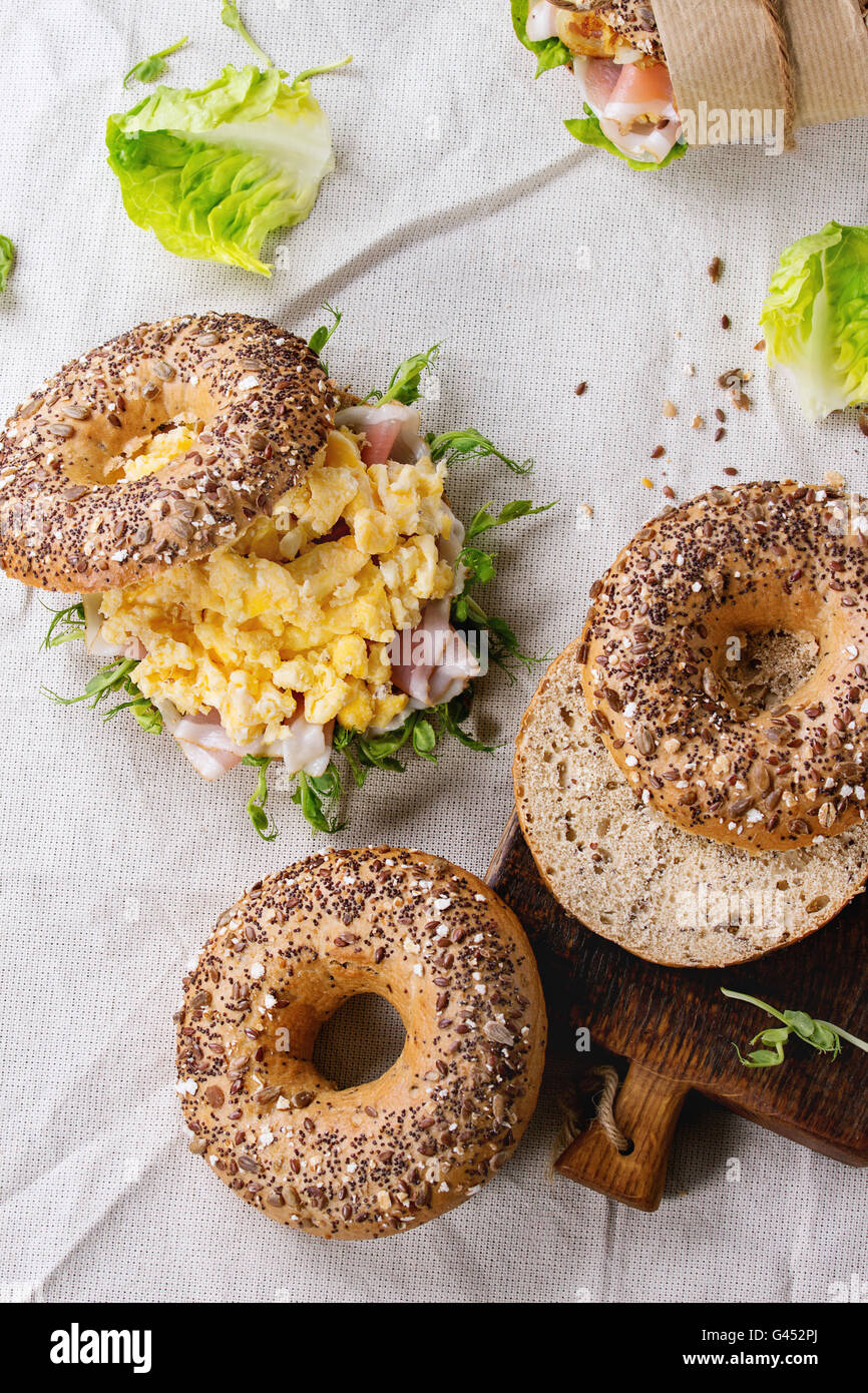 Et vide de grains entiers du personnel des bagels avec œufs brouillés, pousse de pois, oignons frits et jambon prosciutto, décisions sur des nappes blanches Banque D'Images